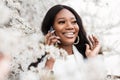 Emotional portrait of a beautiful young black woman with a smile near flowers talking on a smart phone outdoors. Happy smiling Royalty Free Stock Photo