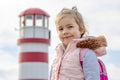 An emotional portrait of a cheerful beautiful blonde girl with a backpack on her shoulders against the background of a sea lightho