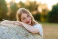 Emotional portrait of a cheerful blonde girl in a countryside landscape with hay rolls in sunset light