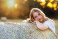 Emotional portrait of a cheerful blonde girl in a countryside landscape with hay rolls in sunset light
