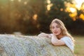 Emotional portrait of a cheerful blonde girl in a countryside landscape with hay rolls in sunset light