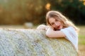 Emotional portrait of a cheerful blonde girl in a countryside landscape with hay rolls in sunset light