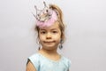 Emotional portrait of a girl in a crown and earrings on a light background. Concept: a little princess, a young fashionista, child