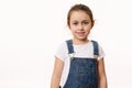 Isolated portrait on white background of a delightful baby girl, wearing blue denim overalls, smiling looking at camera Royalty Free Stock Photo