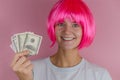 Portrait of a young beautiful happy woman with pink hair holding dollars on a pink background Royalty Free Stock Photo