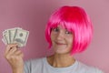 portrait of a young beautiful happy woman with pink hair holding dollars on a pink background Royalty Free Stock Photo