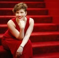 Emotional pretty stylish short-haired woman in red dress sitting on red stairs. Happy elegant playful girl with short haircut sit Royalty Free Stock Photo