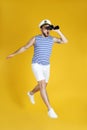 Emotional sailor with binoculars jumping on yellow background