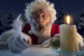 Emotional Santa Claus congratulating with New Year and Christmas, writing a letter, wish list in midnight with candle Royalty Free Stock Photo