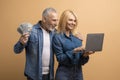 Emotional senior couple using laptop on beige background, showing money Royalty Free Stock Photo