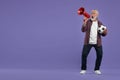 Emotional senior sports fan with soccer ball using megaphone on purple background, space for text