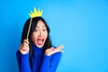 Emotional suprised woman with paper crown on stick on blue background