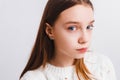 Emotional teen girl in a white knitted sweater on a light gray background.Space for text.