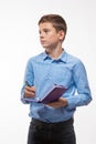 Emotional teenager boy brunette in a blue shirt with a diary and a pen in hand