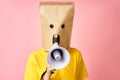 Emotional woman with paper bag on head making announcement with megaphone in hands