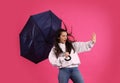 Emotional woman with umbrella caught in gust of wind on pink background