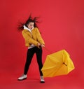 Emotional woman with umbrella caught in gust of wind on red background