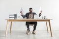 Emotional young black man with documents sitting at desk in front of laptop, feeling triumphant, shouting in excitement Royalty Free Stock Photo