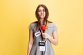 Emotional young girl, female reporter holding reporter microphone isolated on yellow studio background. Concept of