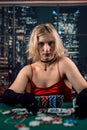 An emotional young lady in a red evening dress is playing cards on a table on green cloth in casino Royalty Free Stock Photo