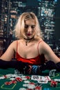 An emotional young lady in a red evening dress is playing cards on a table on green cloth in casino Royalty Free Stock Photo