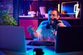 Emotional young man, blogger podcaster with headphones gesturing during recording session in home-studio in neon light.