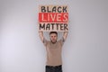 Emotional young man holding sign with phrase Black Lives Matter on light background. End racism