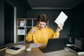 Emotional young man sits at a pulp table with laptop and a book in his hand, looks intently at the laptop screen and nervously Royalty Free Stock Photo