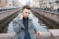 Emotional young man using mobile phone, wearing an elegant gray coat, stands Royalty Free Stock Photo