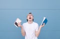 An emotional young man in a white T-shirt and books in his hands is a blue background with a blue background Royalty Free Stock Photo