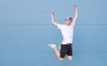 Emotional young man in a white T-shirt jumps against the background of a blue wall and looks at the camera