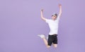 Emotional young man in a white T-shirt jumps against the background of a purple wall and looks at the camera