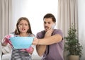 Emotional young woman collecting water leaking from ceiling while her husband calling plumber Royalty Free Stock Photo