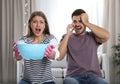 Emotional young woman collecting water leaking from ceiling while her husband calling plumber