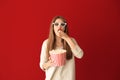 Emotional young woman with cup of popcorn and 3D cinema glasses on color background Royalty Free Stock Photo