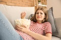 Emotional young woman eating popcorn while watching TV at home Royalty Free Stock Photo