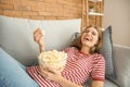 Emotional young woman eating popcorn while watching TV at home Royalty Free Stock Photo