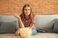 Emotional young woman eating popcorn while watching TV at home Royalty Free Stock Photo