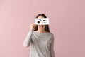 Emotional young woman hiding face behind sheet of paper with drawn eyes on color background Royalty Free Stock Photo