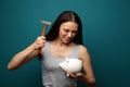 Emotional young woman trying to break a piggy bank with hammer on color background Royalty Free Stock Photo