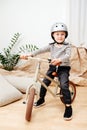 Emotionless little blond boy sitting on a small beige two wheel bike inside room Royalty Free Stock Photo