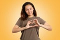 Emotions. Portrait of a Young Caucasian woman with a smile shows a gesture of hearts with her fingers. Yellow background Royalty Free Stock Photo