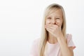 Emotive girl learnt funny word. Studio portrait of joyful adorable european kid with blond hair, covering mouth with Royalty Free Stock Photo