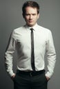 Emotive portrait of serious handsome young man in casual white shirt, black tie, leather belt, gray pants posing over grey Royalty Free Stock Photo