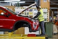 An employee of an automobile plant assembles an engine under the hood of a new car