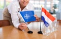 Employee of delegation prepares negotiating table - sets up flag of NATO (OTAN) and Netherlands