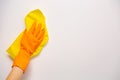 Employee hand in orange rubber protective glove wiping white wall from dust with yellow dry rag. General or regular cleanup.