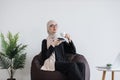 Employee in hijab having coffee break in pouf chair at work