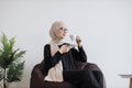 Employee in hijab having coffee break in pouf chair at work