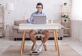 Employee makes a video call with team. Surprised guy in shirt, shorts and socks looks at laptop and gestures